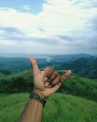 Cropped hand gesturing shaka sign against landscape