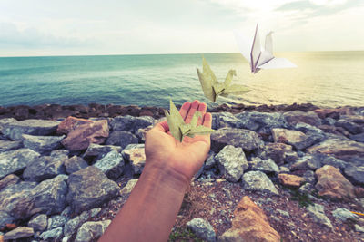 Hand holding rock in sea against sky