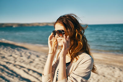 Young woman using mobile phone at beach against sky