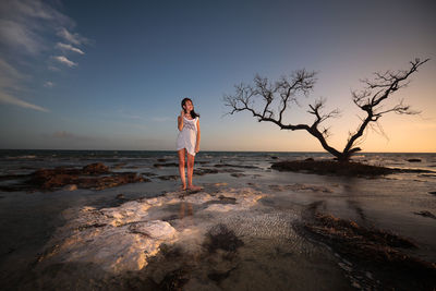 Woman standing on beach against sky during sunset