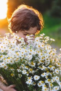 Cute smiling boy at camomile field at sunset in soft sunlight. boy and daisies.