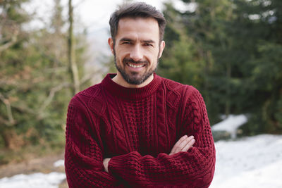Portrait of smiling man with arms crossed standing against forest