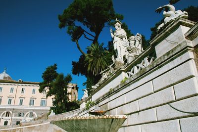 Low angle view of statue against building against clear blue sky