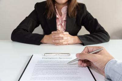 Cropped hand of businessman signing employment contract with employee at desk