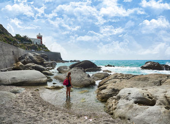 Rear view of person on rock at beach against sky