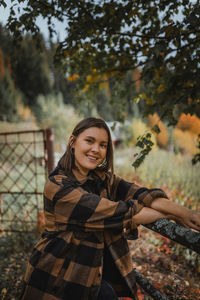 Portrait of smiling young woman standing against fall trees