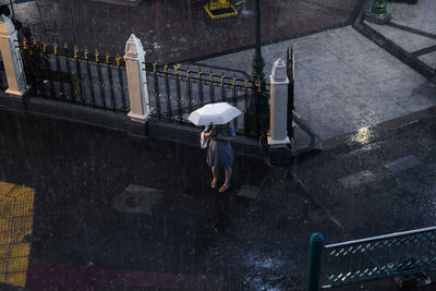 High angle view of woman with umbrella standing in rain by gate