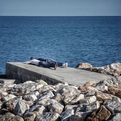 Lounge chairs on rocks by sea against clear sky