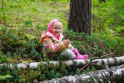 Smiling girl sitting in cranberry in forest
