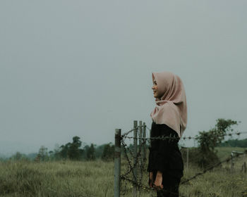 Side view of woman in headscarf standing on field against clear sky