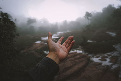 Cropped hand gesturing against sky during foggy weather