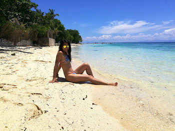 Woman relaxing on beach against sky