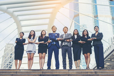 Smiling young colleagues with arms crossed standing on footpath against buildings in city