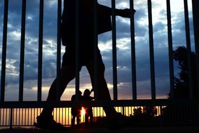 Silhouette man standing by window against sky during sunset