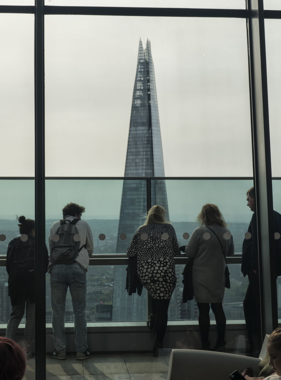 REAR VIEW OF PEOPLE WALKING IN CITY AGAINST SKY