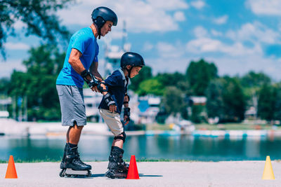 Grandfather holding grandson while rollerblading by lake