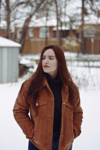 Young woman looking away while standing on snow covered field