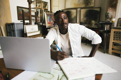 Contemplative male designer with diary and laptop on table at workplace