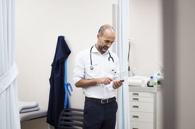 Doctor using smart phone while standing in room at hospital seen through door