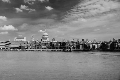 Thames river and buildings in city against cloudy sky