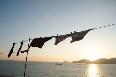 Clothes drying on rope against sea during sunset