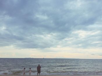 People standing on beach against sky during sunset