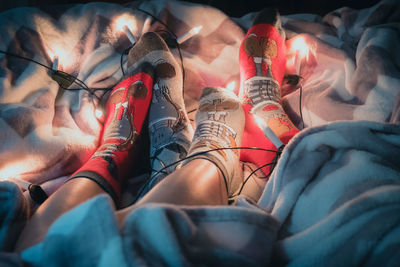 Low section of people wearing socks with illuminated string lights sitting on bed