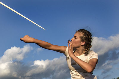 Low angle view of athlete throwing javelin against blue sky