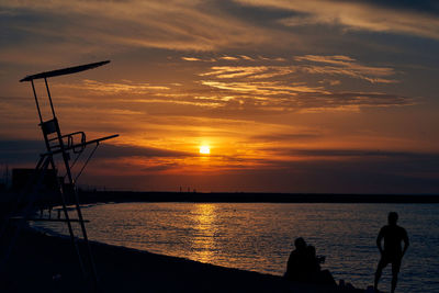 Silhouette people on sea against sky during sunset