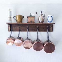 Saucepans and utensils hanging from hooks below shelf on wall in kitchen at home