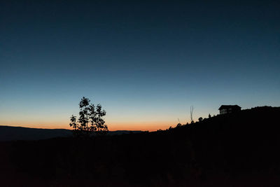 Silhouette trees on landscape against clear sky