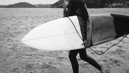 Midsection of man with surfboard walking against sea