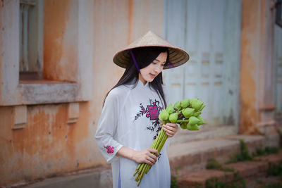 Woman with flowers standing against wall