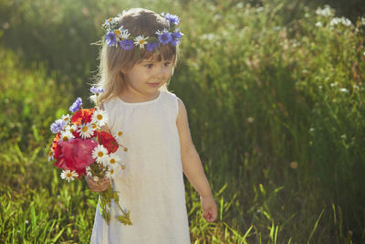 Charming child in linen dress walks in a field with flowers at sunset