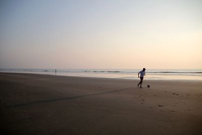 Full length of man playing with ball at beach against clear sky