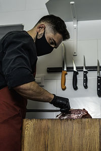 Butcher with mask cutting raw meat in the wood