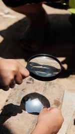 Cropped hand holding magnifying glass over paper