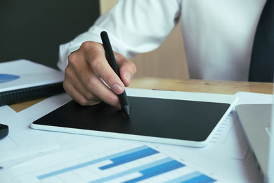 Midsection of businessman working on digital tablet at desk