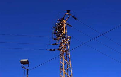 Low angle view of electricity pylon against blue sky