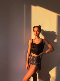 Young woman standing against wall during sunny day