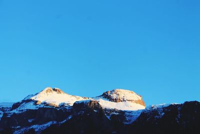 Low angle view of snow mountains against clear blue sky