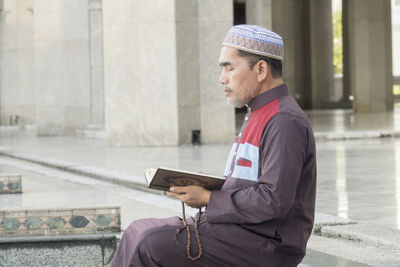 Mature man reading koran while sitting at mosque