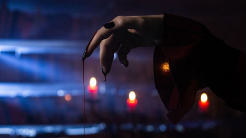 Close-up of human hand against illuminated string lights