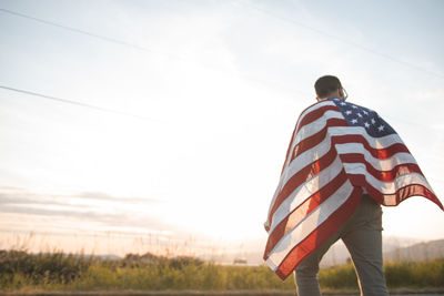 Man holding american flag while standing on field against sky