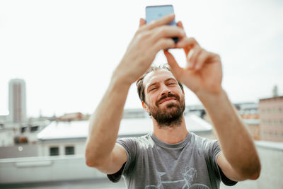 Smiling mid adult man taking selfie with smart phone in city