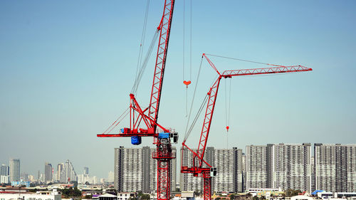 Low angle view of cranes against buildings