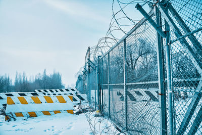 Snow covered fence against sky during winter