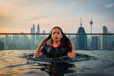 Woman swimming in infinity pool against city