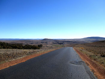 Road leading towards mountains against clear blue sky