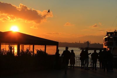 Silhouette people on river against sky during sunset